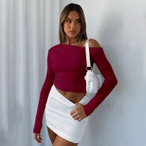 Modell trägt ein burgunderrotes asymmetrisches Langarm-Crop-Top mit stilvollem Schulterdetail