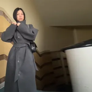 Modella asiatica con cappotto di lana grigio con cintura in un elegante vano scale