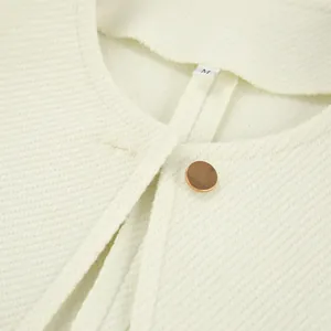 Detailaufnahme einer cremefarbenen Tweedjacke mit Textur und goldenem Metallknopf