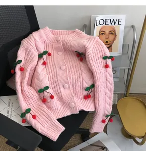 Close-up of pink knitted cardigan with 3D cherry appliques and cable knit texture