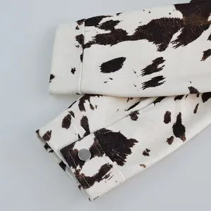 Gedetailleerde opname van de manchet van jas met koeprint, zilveren knoop en stiksels