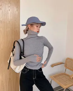Close-up of a grey ribbed turtleneck knit sweater worn with a blue cap and tote bag.