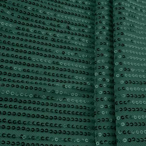 Macro close-up of emerald green sequin fabric showing texture and stitching detail.