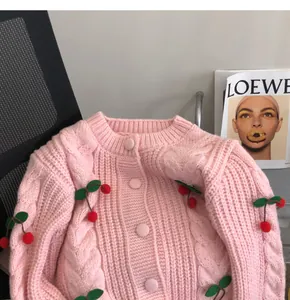 Close-up detail of pink knitted cardigan featuring 3D cherry accents and cable knit patterns.