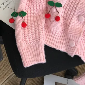 Close-up of pink chunky knit cardigan featuring cute 3D red cherry applique decorations