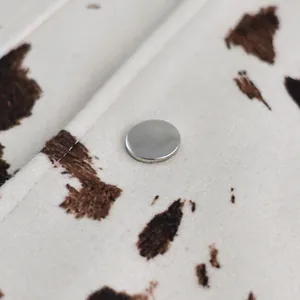 Detailopname van een zilveren metalen knoop op een herfstjas met een koeienprint textuur.