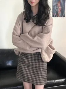 Détail d'un pull en maille à col rond ample avec une jupe à carreaux en intérieur