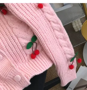 Detailed view of a sweet pink knitted cardigan featuring 3D cherry pom-pom accents