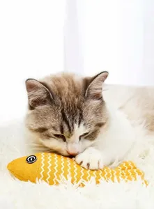 Gros plan d'un chat mordant un jouet jaune en forme de poisson rempli d'herbe à chat.