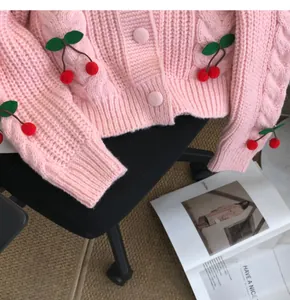 Detail of a pink knitted cardigan featuring 3D cherry appliques and cable knit texture.