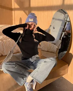 Model wearing a black turtleneck ribbed knit sweater with blue jeans in cozy bedroom