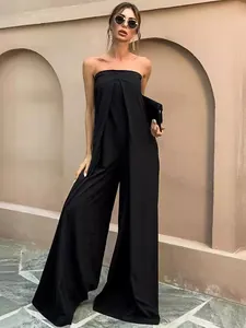 Élégante combinaison pantalon bustier noire à jambes larges sur fond de mur beige.