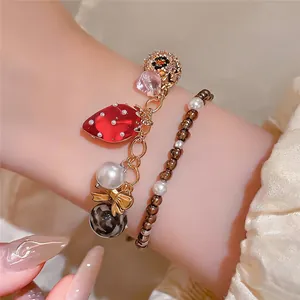 Gros plan d'un ensemble de bracelets à pendentif fraise et perles sur un poignet.