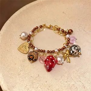 Gros plan d'un bracelet en perles avec breloque fraise, cœur et nœud papillon doré.