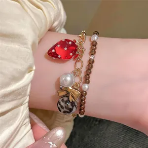 Vue détaillée d'un ensemble de bracelets avec pendentif fraise et perles nacrées.