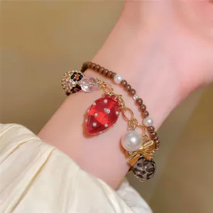 Vue détaillée d'un bracelet en perles de style doux avec un pendentif fraise rouge.