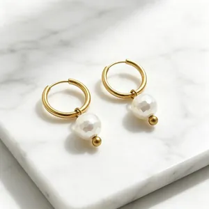 Gros plan sur des boucles d'oreilles créoles dorées avec perles de nacre à facettes blanches