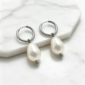 Gros plan de boucles d'oreilles créoles avec perles en forme de larme sur fond marbre.