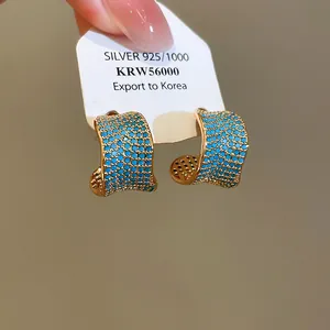 Dettaglio degli orecchini a forma di C placcati in oro 18 carati con zirconi blu vibranti.