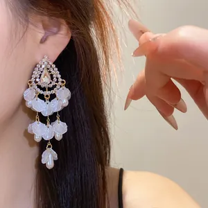 Detalle de elegantes pendientes vintage con pedrería, perlas y colgantes de pétalos de nácar