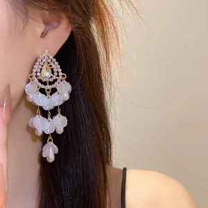 Primer plano de elegantes pendientes con pedrería y borlas de concha blanca en la oreja