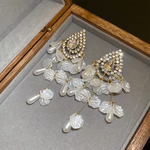 Vista detallada de pendientes con pedrería, perlas y pétalos de nacre en un estuche de madera