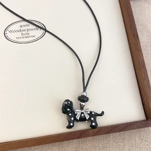 Detail of a black enamel dog pendant necklace with white polka dots and a silver bow