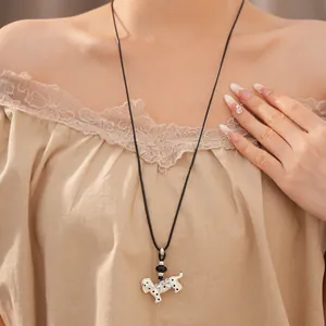 Close-up of a stylish dalmatian dog pendant necklace on a model with a beige lace top.