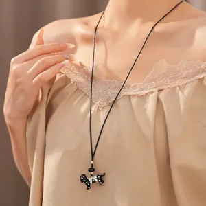 Close-up of a long black cord necklace featuring a polka dot dog pendant with a white bow.