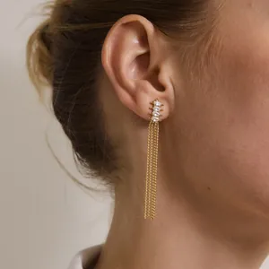 Détail de boucles d'oreilles à pompons dorés avec pierres blanches marquise