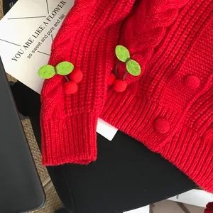 Close-up detail of a cute cherry applique on a vibrant red cable knit cardigan sweater
