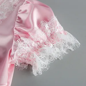 Detail view of a pink satin puff sleeve featuring intricate white lace trim embroidery