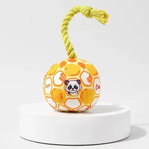 Close-up of yellow plush dog ball toy with cotton rope tail and panda pattern.