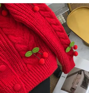 Macro close-up of red cable-knit sweater detail featuring cute 3D cherry appliqués