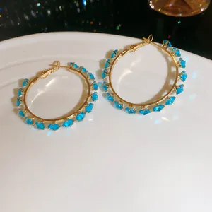 Close-up of gold hoop earrings featuring sparkling blue zircon stones on a white plate.