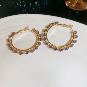 Elegant gold hoop earrings featuring sparkling faceted purple zircon crystals on a white plate