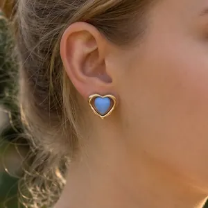Primer plano de un pendiente de corazón de esmalte azul en la oreja de una modelo.