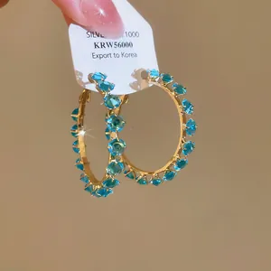Detailed close-up of light luxury gold hoop earrings with sparkling blue zircon crystals.