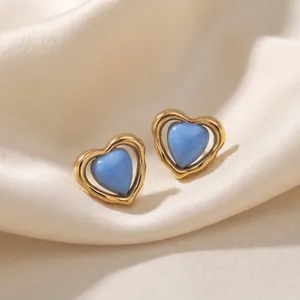 Primer plano de pendientes de corazón minimalistas en esmalte azul y marco dorado