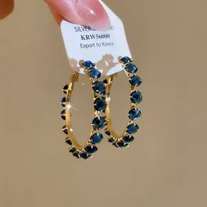 Detail view of sparkling gold-tone hoop earrings set with dark blue zircon crystals.