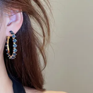 Close-up of elegant gold hoop earrings with blue zircon stones worn on model's ear