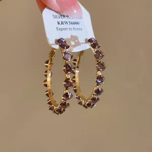 Detail of gold-plated hoop earrings with dark purple zircon studs and silver 925 tag