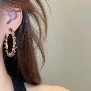 Close-up shot of elegant golden hoop earrings with sparkling zircon stones on ear