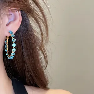 Close-up of sparkling blue zircon hoop earrings on model's ear with warm background