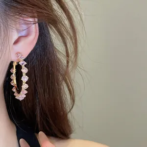 Close-up of elegant pink zircon gold hoop earrings worn on an ear for detail view