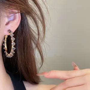 Macro close-up of sparkling zircon hoop earrings on a model with an elegant gold-tone finish.