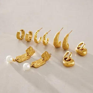 Detalle de pendientes de acero inoxidable dorados con texturas martilladas y de arena.