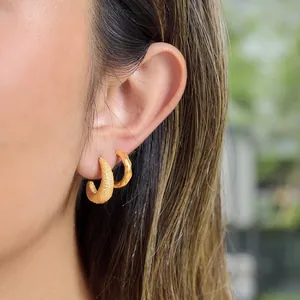 Primer plano detallado de pendientes de aro con acabado dorado texturizado y martillado