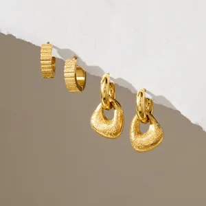Vista detallada de pendientes de acero dorado con texturas acanaladas y martilladas