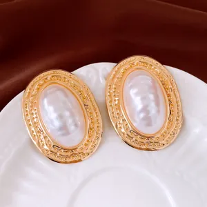 Makroansicht eleganter goldener Perlenohrstecker mit Struktur auf einem weißen Porzellanteller.
